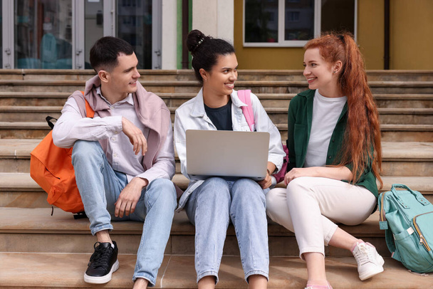 Happy young students studying together with laptop on steps outdoors - Photo, Image