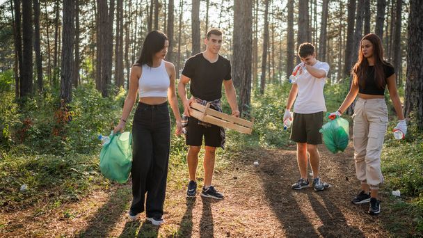 grupo de amigos adolescentes gen Z homens brancos masculinos e femininos mulheres pegando lixo garrafas de plástico e papel da floresta limpeza da natureza em dia ensolarado conceito ecologia cuidado ambiental - Foto, Imagem