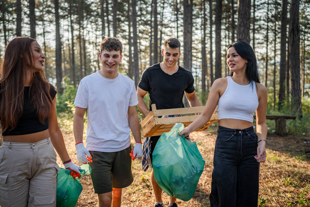 csoport tizenéves barátok gen Z férfi és női kaukázusi férfiak nők felvette hulladék műanyag palackok és papír az erdőben takarítás természet napsütéses nap környezetvédelem ökológia koncepció - Fotó, kép