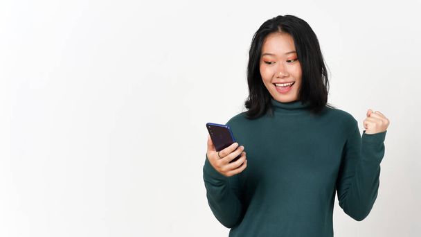 Smartphone halten Blick auf Smartphone mit glücklicher Ja-Geste der schönen Asiatin isoliert auf weißem Hintergrund - Foto, Bild