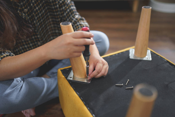 Frauen verwenden Schraubendreher, um Schrauben anzuziehen, während sie Stuhlbein zum Möbelbau zusammenbauen. - Foto, Bild