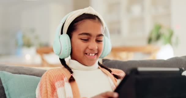 Girl, kid and tablet with headphones on sofa for online video games, watching funny movies and play educational app. Happy child laugh with digital technology, listening to music or streaming cartoon. - Footage, Video
