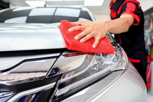 Aziatische jonge werknemer gebruik maken van microvezel doek voor het reinigen en polijsten van auto 's in auto polijsten kamer. Onderdeel van autowasdiensten. Selectieve focus op de hand. - Foto, afbeelding