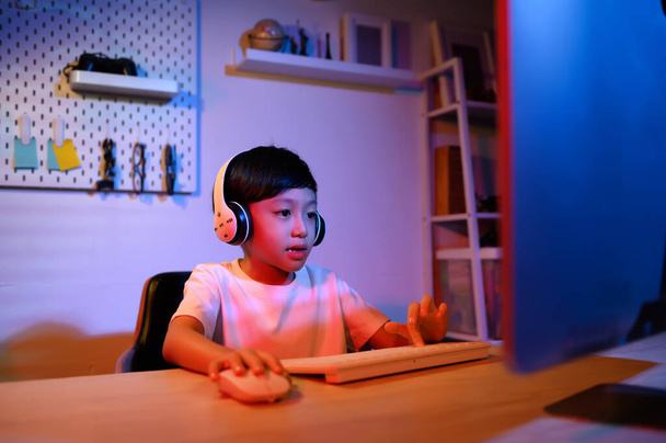 Asian Kid Boy intenta Gaming Stream en el escritorio de la computadora para la diversión y el entretenimiento en el hogar, explorando el viaje virtual del juego del mundo. Desarrollar habilidades a través del juego, la transmisión y el vlogging para niños - Foto, Imagen