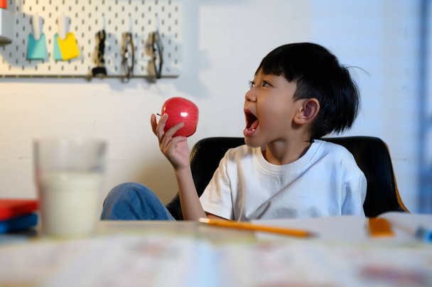 Estudiante asiática sostiene fruta de manzana y juega después de aprender a refrescarse en el hogar, educación temprana, estudio y hábitos saludables en el hogar. - Foto, Imagen