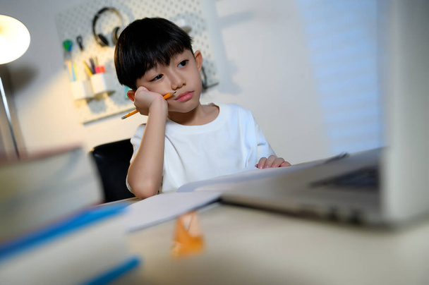 Asiático crianças menino tédio e sonolento aprendizagem, mão segurando lápis e queixo descansando em estudar sozinho em casa com ferramentas digitais laptop. - Foto, Imagem
