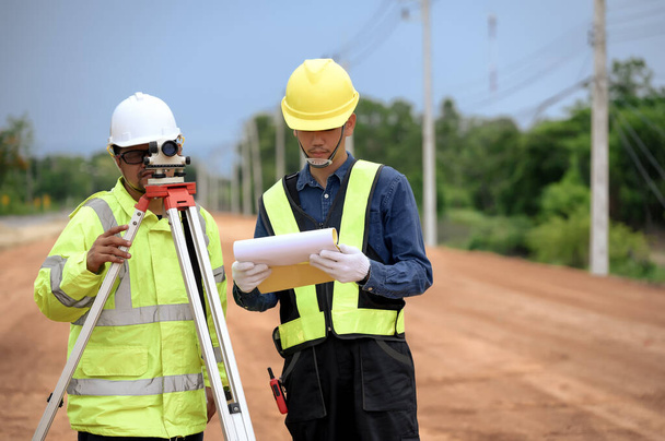 Asijský zeměměřič inženýr dva lidé kontrolu úrovně půdy s Surveyor zařízení dalekohledu pro měření vyrovnání pro řezání a výplň, začal vyrovnávat půdu na staveništi dálnice. - Fotografie, Obrázek