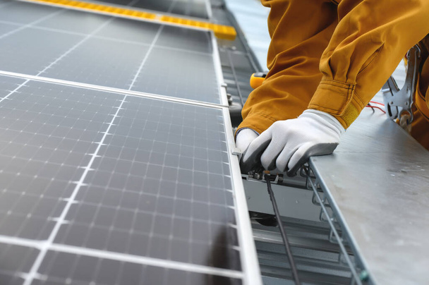 Technik noszący odzież ochronną podczas instalacji panelu słonecznego lub fotowoltaicznego punktu wsparcia w dzień na budynkach fabrycznych na dachu. - Zdjęcie, obraz