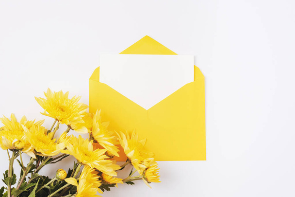 Yellow envelope with blank card and flowers on white background. Birthday, invitation, holiday concept. Top view, flat lay, mockup. - Photo, Image