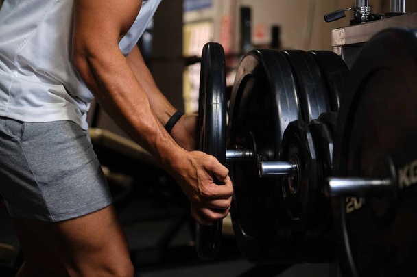 Unrecognizable strong man putting in place weight plate at a gym. - Photo, Image