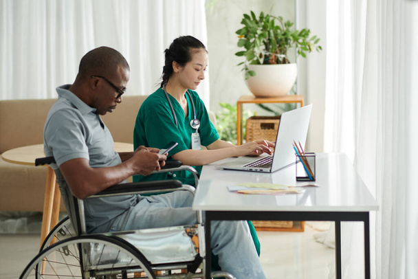 Patiënt met een handicap sms 'en vrienden wanneer maatschappelijk werker werkt op laptop naast hem - Foto, afbeelding