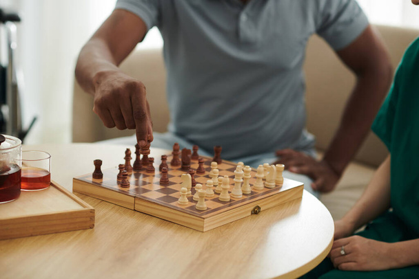 Imagen de primer plano del peón en movimiento del paciente al jugar al ajedrez con la enfermera médica - Foto, Imagen