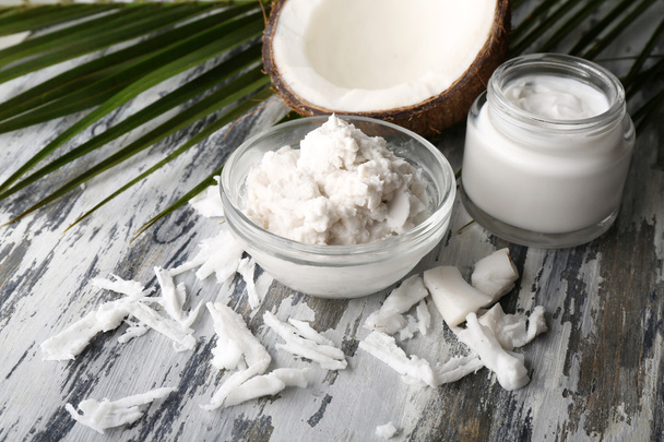 Coconut with coconut oil in bowl with jar of cosmetic cream on wooden background - Fotoğraf, Görsel