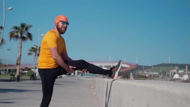A kocogó férfi felmelegíti a térdízületet, mielőtt edzést tartana a futópályán. Egészséges életmód felnőtteknek. Fitnesz edzés reggel munka előtt - Felvétel, videó
