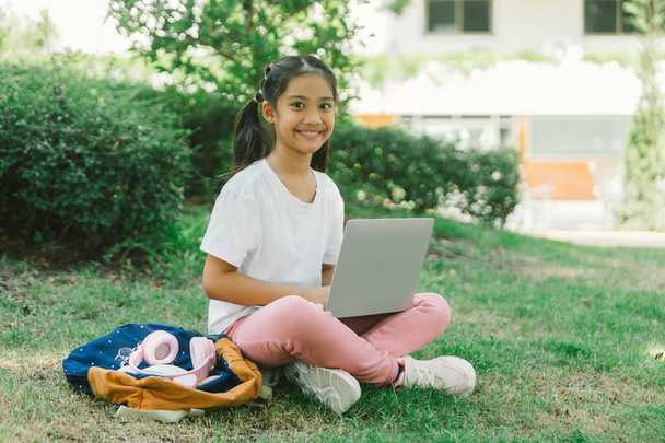 Cute asian child girl using laptop sitting on grass in the park. - Photo, Image