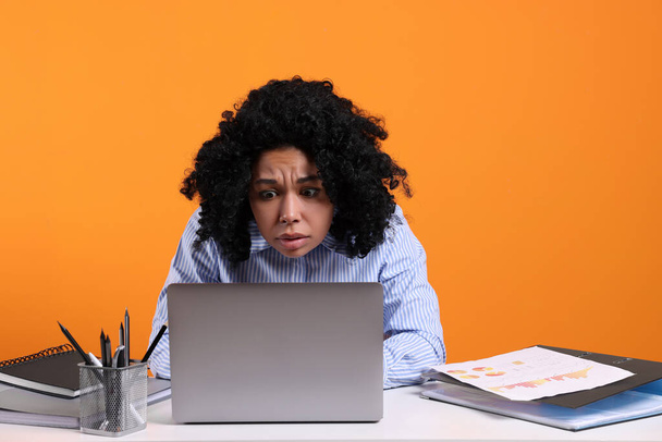 Stressful deadline. Sad woman looking at laptop at white table on orange background - 写真・画像
