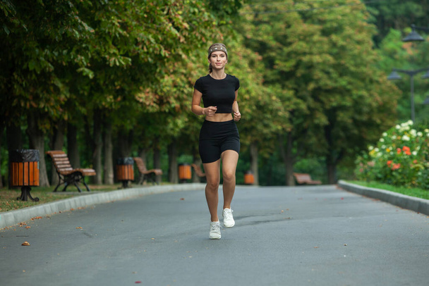 Athletic young woman in sportswear jogging in the park. Fitness and healthy lifestyle. Portrait of a beautiful young woman in sportswear outdoors. Sport fitness model caucasian ethnicity training outdoor. - Photo, Image
