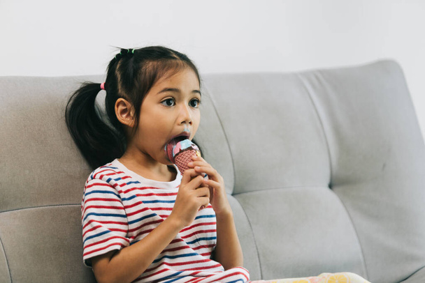 aranyos ázsiai kislány eszik fagylalt kanapén otthon - Fotó, kép