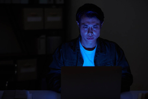 Портрет серьезного разработчика программного обеспечения, работающего на ноутбуке в темной комнате ночью - Фото, изображение