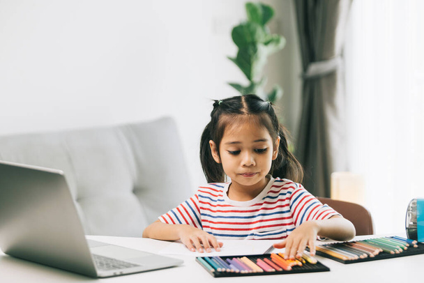 Schattig klein Aziatisch meisje met behulp van laptop en het doen van huiswerk thuis. - Foto, afbeelding