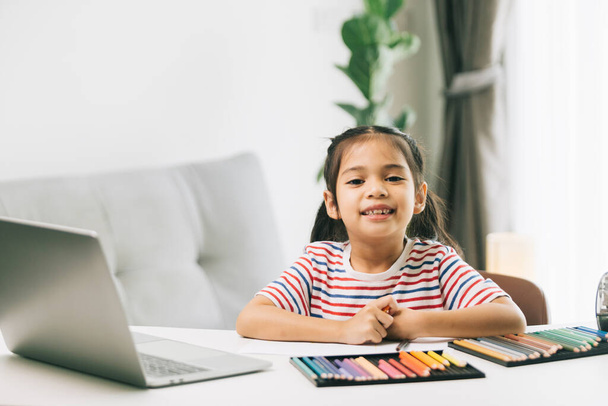Little asian girl drawing with color pencils and laptop at home - Photo, Image