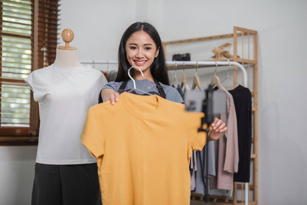 Азіатська пара спілкується в прямому ефірі, щоб продавати одяг і показувати одяг клієнтам під час продажу вдома.. - Фото, зображення