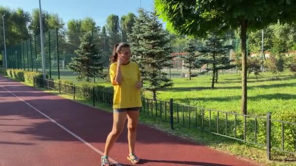 Multiraciální mladá žena se vydá na běh na běžeckou stezku ve veřejném parku. Zastaví se, zvedne sluchátko a za slunečného rána si popovídá bezdrátovými sluchátky. Aktivní životní styl podnikatelky - Záběry, video