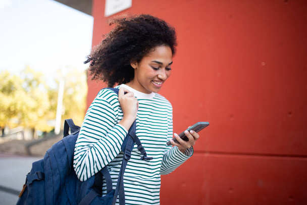 Portrait étudiant féminin marchant avec sac et regardant le téléphone mobile - Photo, image