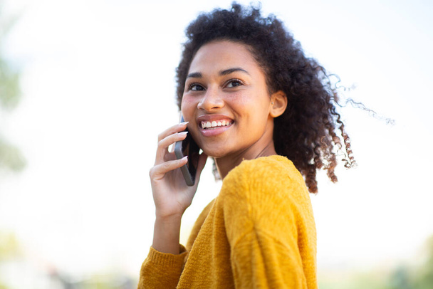 携帯電話で話す若いアフリカ系アメリカ人女性を笑顔にするポートレートを閉じる - 写真・画像