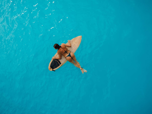 Surf girl en bikini nadando con tabla de surf en océano turquesa. Vista aérea de la mujer surfista - Foto, Imagen