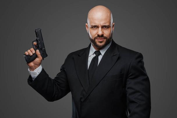 Commanding portrait of a bald, bearded gentleman with a gun, dressed sharply in formal attire - Photo, Image