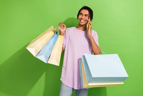 Photo of handsome guy shopper hold mall shopping bags speak telephone isolated on green color background. - Foto, imagen