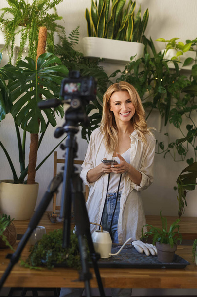 Stijlvolle bloemist en blogger vastleggen van haar plant zorg routine in de kamer met levendige groen - Foto, afbeelding