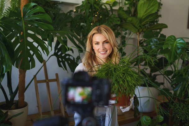 Elegante florista y blogger capturando su rutina de cuidado de plantas en la habitación con una vibrante vegetación - Foto, Imagen