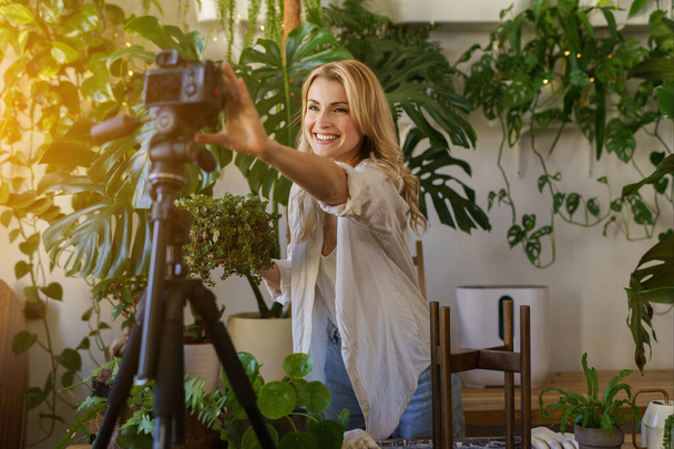 Stijlvolle bloemist blogger vastleggen van haar plant zorg routine in een zonovergoten kamer met levendige groen - Foto, afbeelding