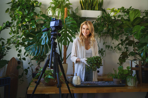 Stylowy kwiaciarnia i blogger przechwytywanie jej pielęgnacji roślin rutynowych w pokoju z żywą zielenią - Zdjęcie, obraz
