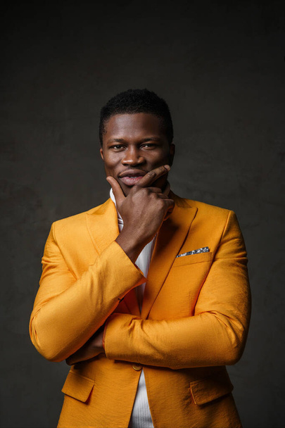 Portrait of a smartly dressed black man in a yellow blazer with short hair against a dark backdrop - Photo, Image