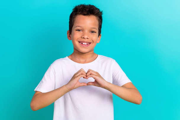 Portrait of grateful kind boy wear stylish white clothes fingers demonstrate heart shape isolated on cyan color background. - Фото, изображение