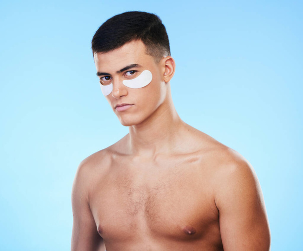 Man, beauty and portrait with eye patch for skincare, grooming and clean with hygiene on blue background. Skin treatment, cosmetics product and wellness, self care and dermatology in a studio. - 写真・画像