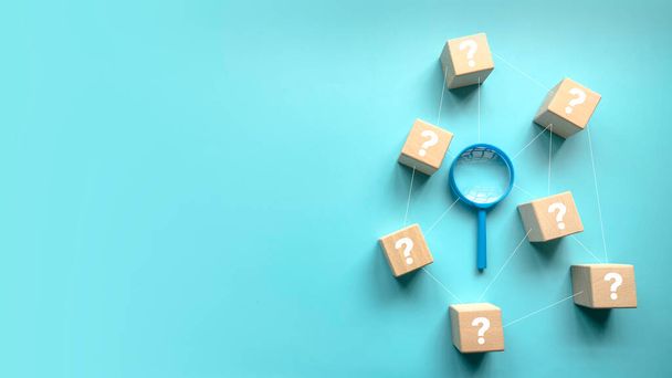 QnA or questions and answers concept. Blue magnifying glass with question symbol on wooden cube over a blue background with copy space . - Photo, Image
