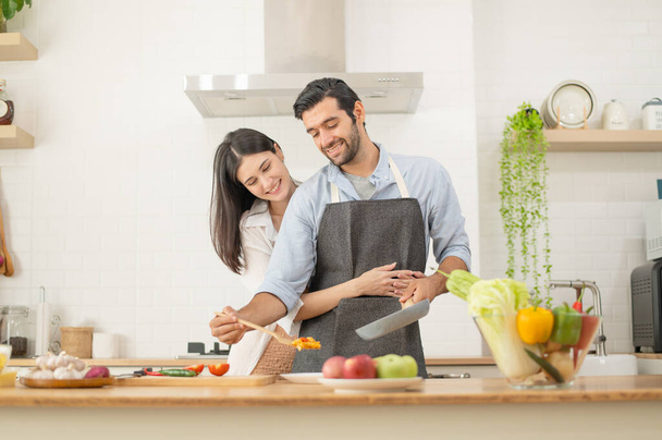 Szczęśliwa para przygotowuje jedzenie w domu, młoda para kroi warzywa razem na blacie kuchennym, mężczyzna i kobieta zakochani - Zdjęcie, obraz