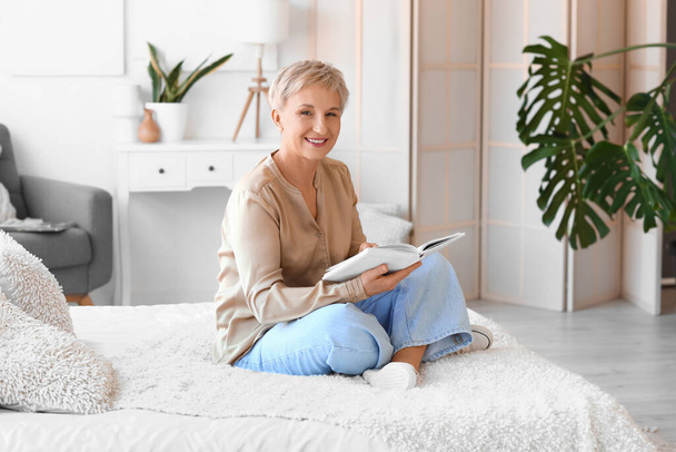 volwassen vrouw lezen boek in slaapkamer - Foto, afbeelding