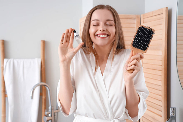 Mujer joven con suero para el tratamiento de pérdida de cabello y cepillo en casa - Foto, Imagen