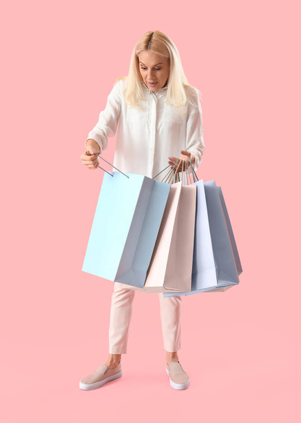 Šokovaná dospělá žena s papírovými taškami na růžovém pozadí. Online nakupování - Fotografie, Obrázek