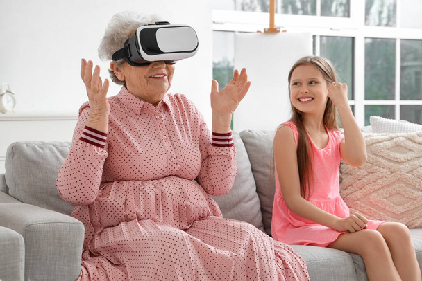 Маленькая девочка и ее бабушка используют виртуальные очки дома - Фото, изображение