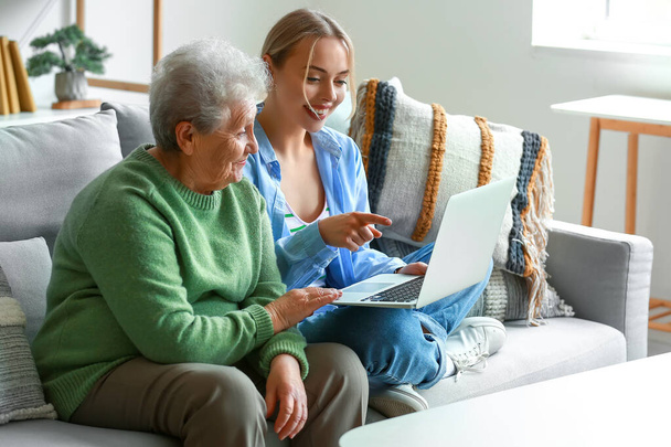Jonge vrouw met haar oma met behulp van laptop thuis - Foto, afbeelding