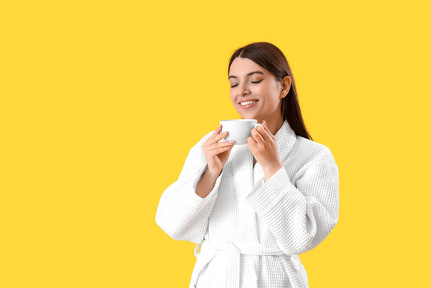 fiatal nő köpenyben csésze kávé sárga háttér - Fotó, kép