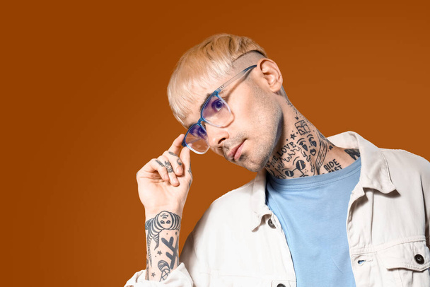 Jeune homme tatoué dans des lunettes élégantes sur fond de couleur, gros plan - Photo, image