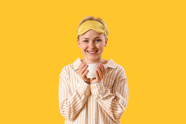 Young woman in pajamas with cup of coffee on yellow background - Photo, Image