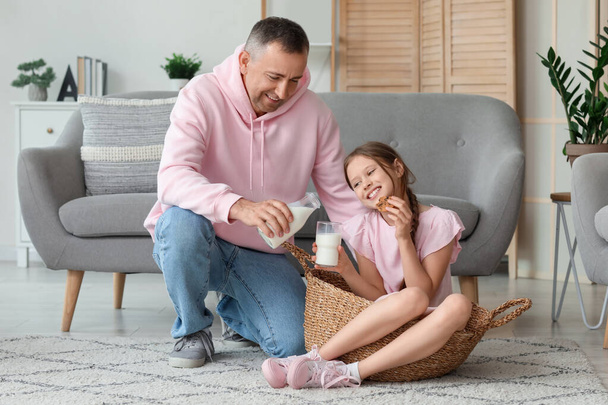 Маленькая девочка с отцом сидит на полу и пьет молоко в гостиной - Фото, изображение